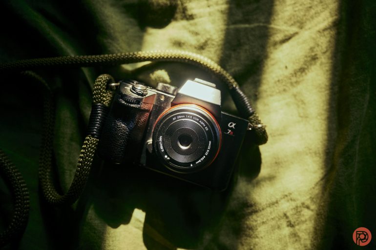 A Sony α7 camera with a lens and green strap rests on a textured green surface in sunlight.