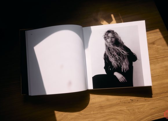 An open book on a wooden table shows a black-and-white portrait of a woman with long, wavy hair.
