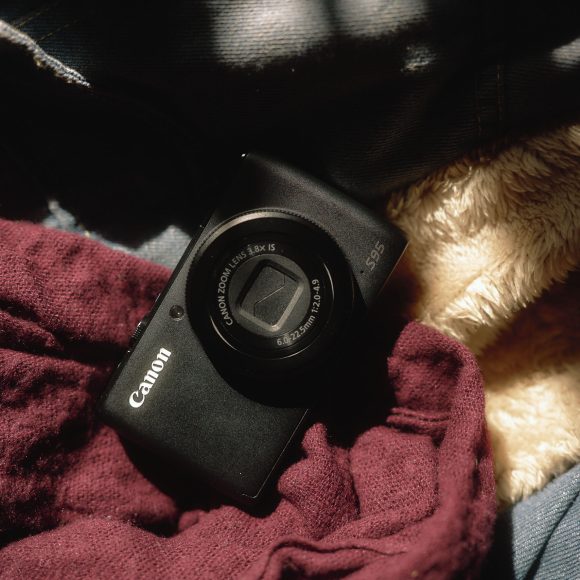 Canon camera placed on a bed of soft fabrics in warm, dappled light.