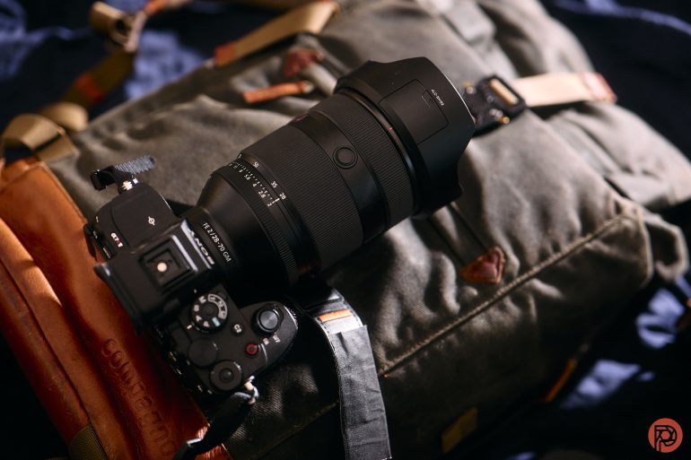 Camera with large lens resting on a green and brown backpack.