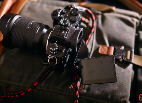 A digital camera with a flip-out screen rests on a green camera bag with leather accents.