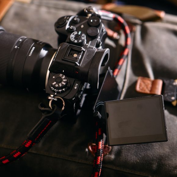 A digital camera with a flip-out screen rests on a green camera bag with leather accents.
