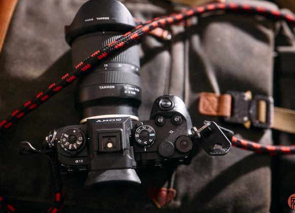 Sony camera with Tamron lens and red-black strap resting on a dark fabric bag.