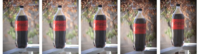 A Coca-Cola bottle on a ledge, captured with a DIY camera, gradually unfocused from left to right.