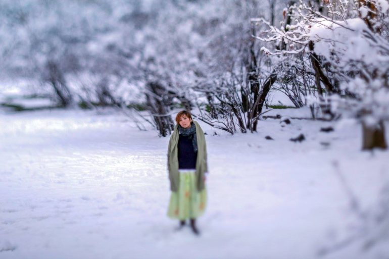 Amidst a snowy landscape, where snow-covered trees paint the backdrop, a person stands gracefully in a green skirt and scarf. Capturing this serene moment could easily inspire those interested in DIY cameras to craft their own photographic memories.