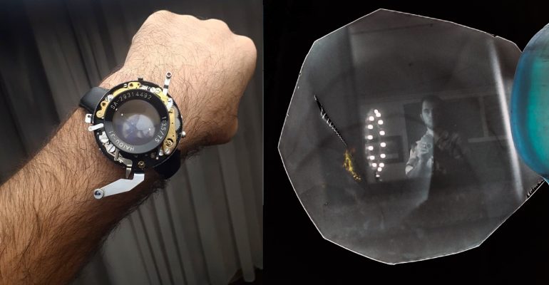 A hand wearing a camera lens-themed wristwatch, reminiscent of DIY cameras. A vintage photo with reflection on the right.