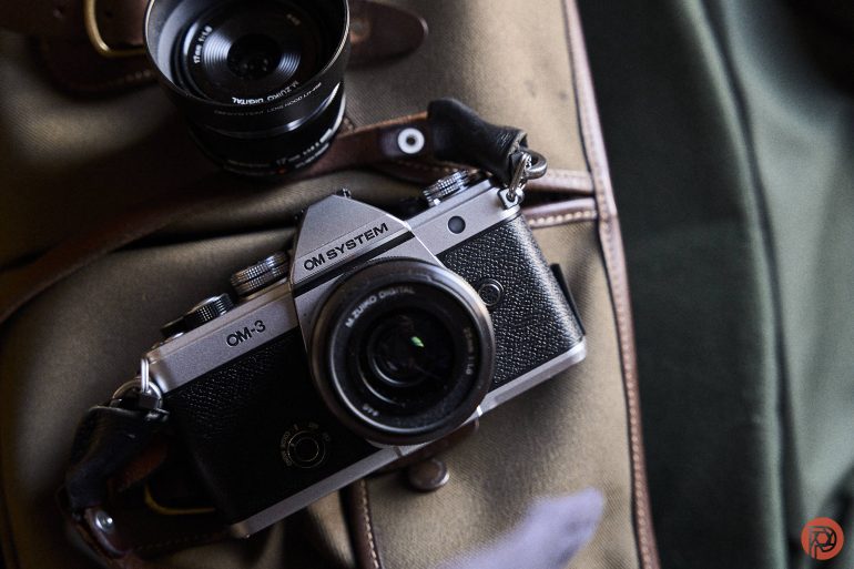 The Vintage looking OM-3 camera on a bag, with a detached lens nearby.