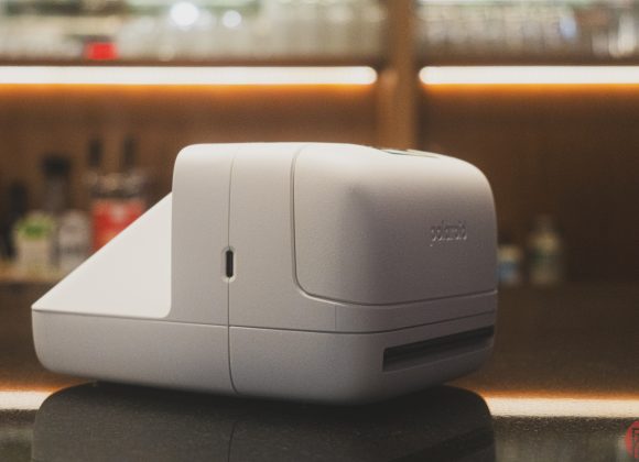 White Polaroid label printer on a reflective countertop with blurred background.