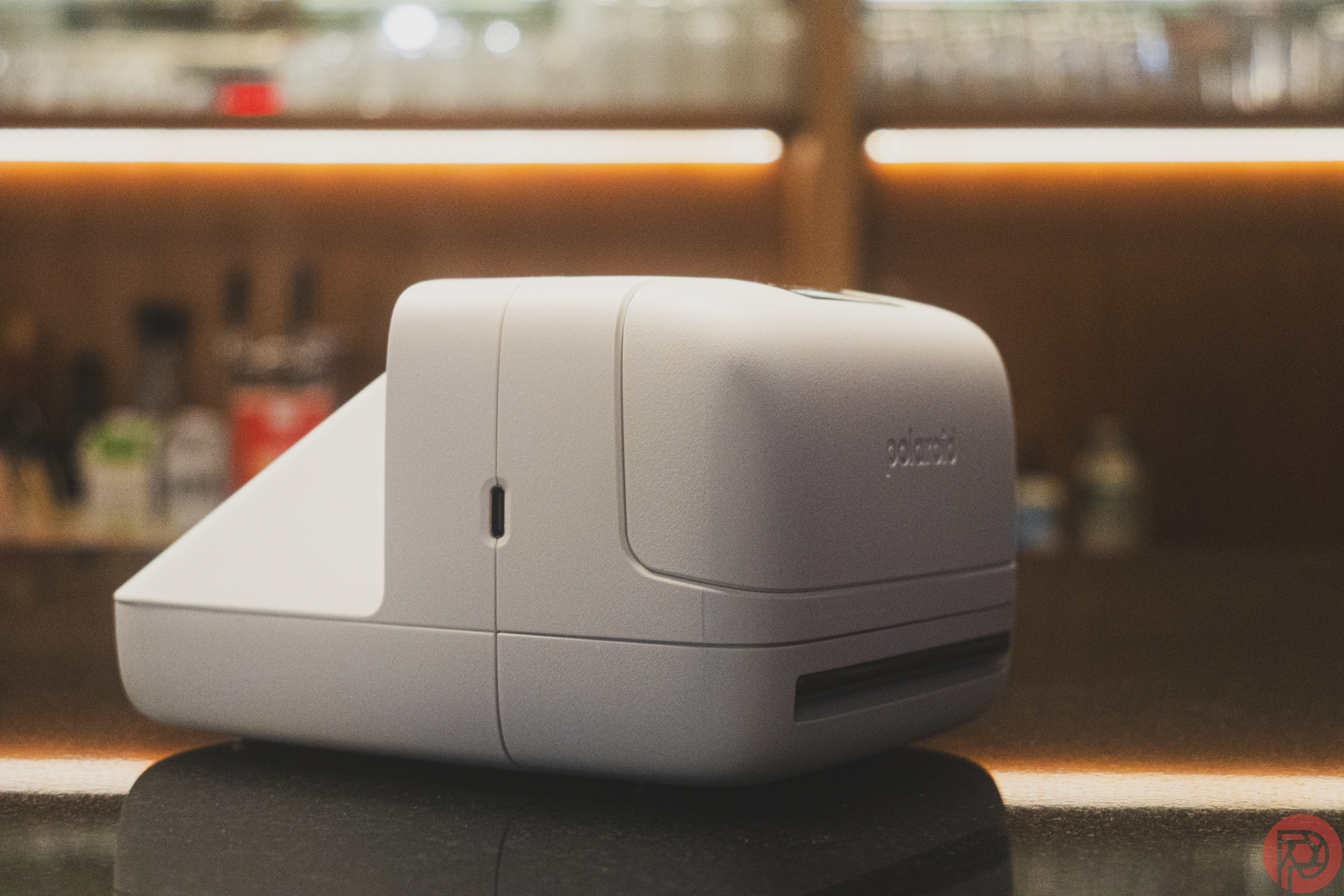 White Polaroid label printer on a reflective countertop with blurred background.