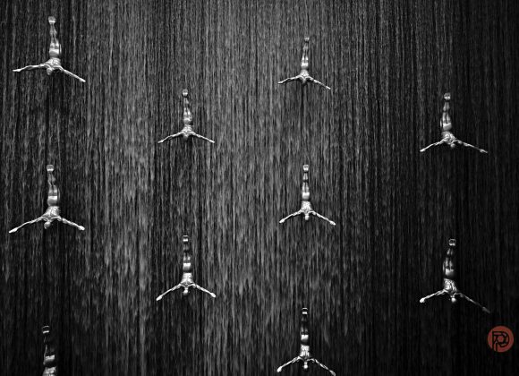 Statues of divers in freefall pose on a large indoor waterfall wall.