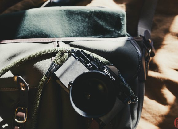 A Nikon camera rests on a green bag, with sunlight casting shadows.