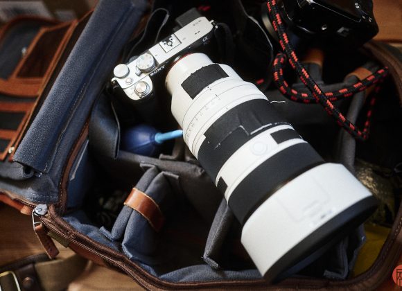 Camera bag with a Sony camera, large white telephoto lens, and accessories inside padded compartments.