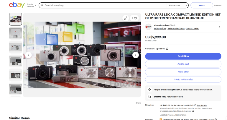 A collection of rare Leica compact cameras displayed on a table in front of a colorful background.
