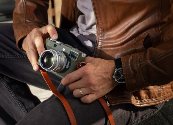 Person in a brown leather jacket holding a vintage camera with a leather strap on their lap.