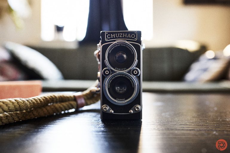 A vintage Chuzhao twin-lens camera sits on a dark wooden table with a rope strap beside it.
