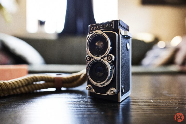 A vintage CHUZHAO twin-lens camera sits on a dark table with a blurred background.