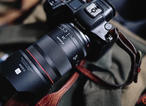 Close-up of a Canon EOS camera with a 24mm lens resting on a green and brown fabric surface.