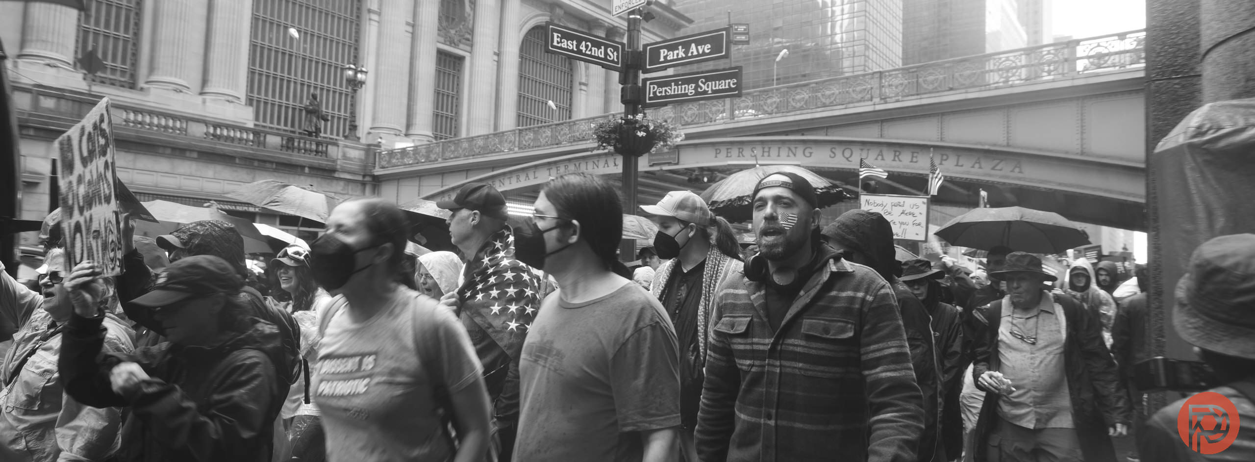 A large group of masked people march in the rain near Park Ave and Pershing Square in New York City.