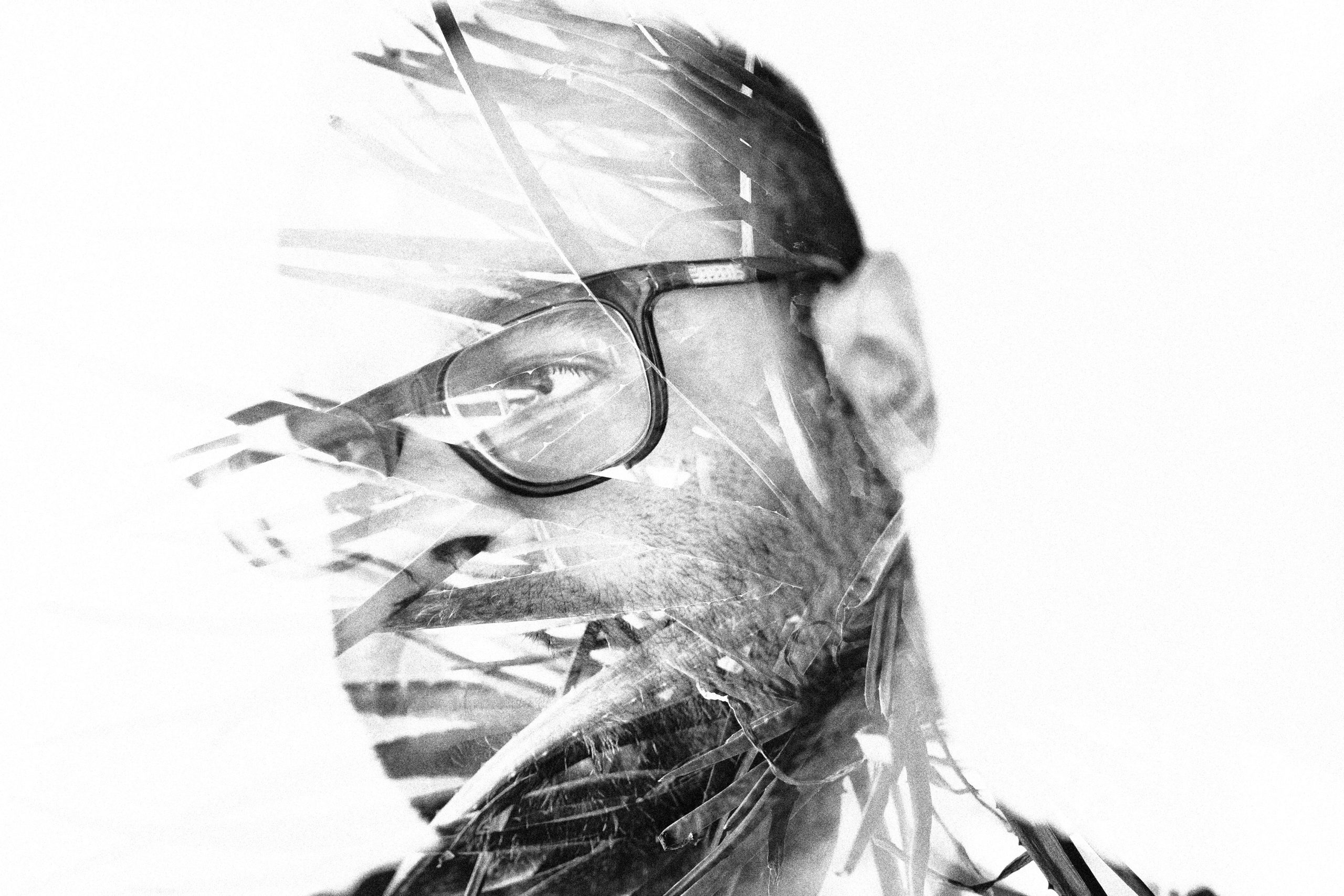 Don't Let Your Camera Make Photos For You Black and white double exposure of a man wearing glasses overlaid with abstract palm leaves.