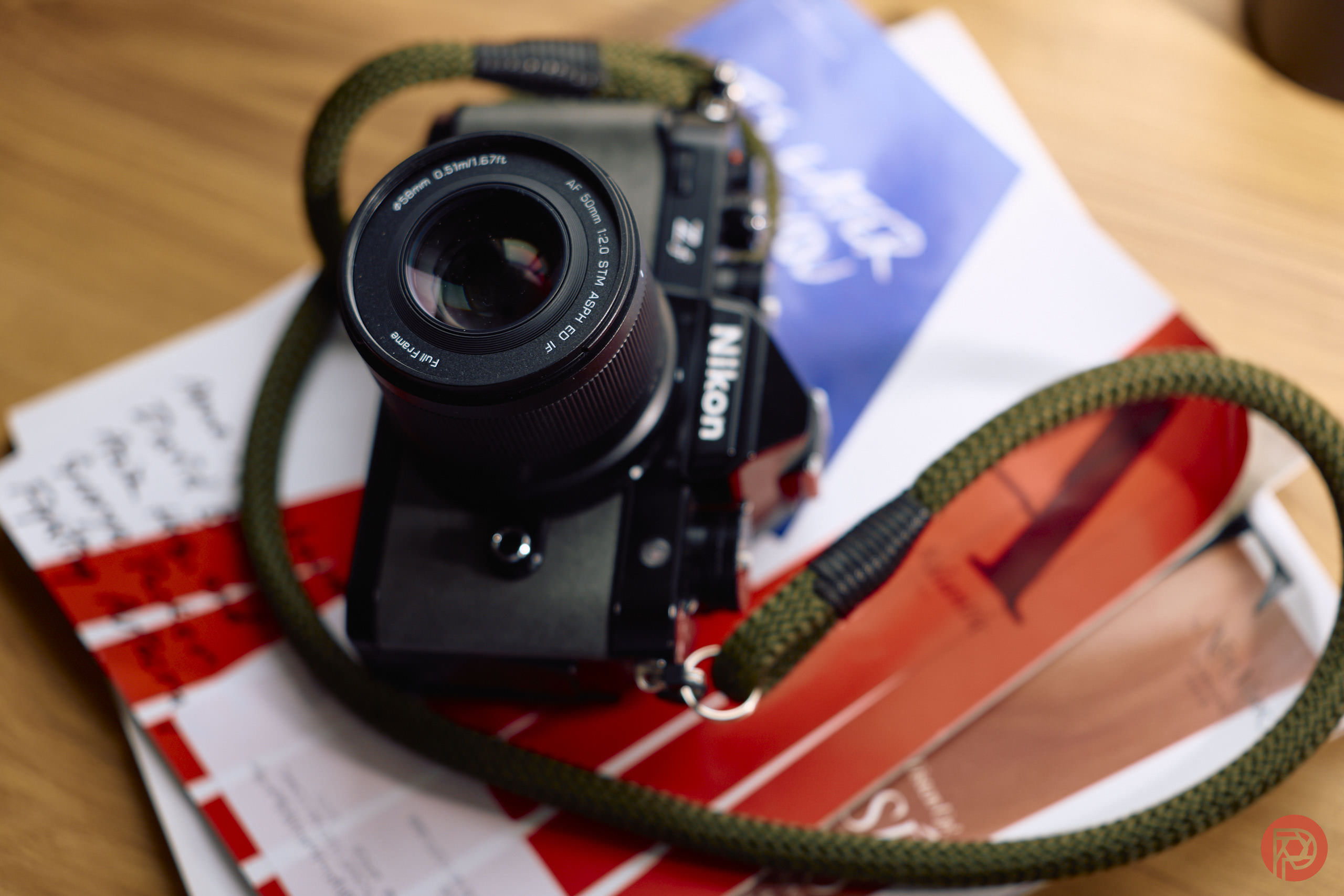 A Nikon camera with a green strap lies on top of a stack of magazines on a wooden surface.