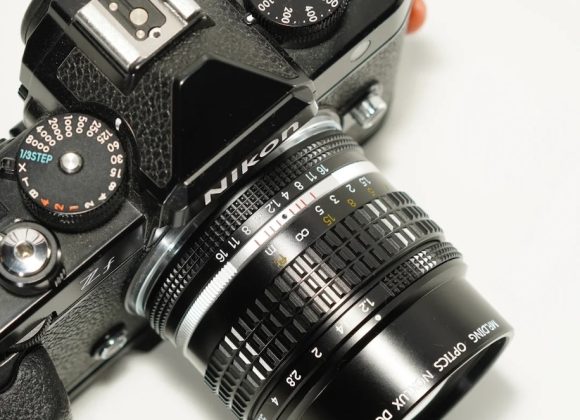 A close-up of a vintage Nikon film camera with a 50mm lens on a white surface.