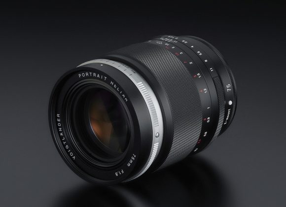 A camera lens with manual focus and aperture rings is placed on a dark, reflective surface.
