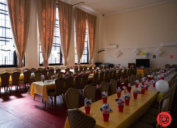 Long tables with yellow tablecloths and party favors in a decorated room with large windows and curtains.