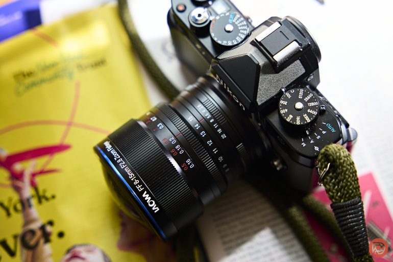 A black camera with a VOIGTLANDER lens rests on an open magazine with colorful pages.