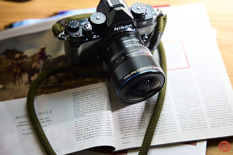 A Nikon camera with a green strap rests on an open magazine on a wooden surface.