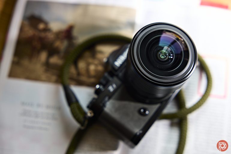A digital camera with a green strap rests on an open magazine or newspaper.