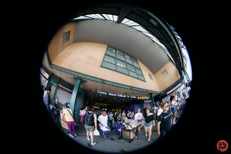 People exit the Coney Island-Stillwell Ave subway station, captured with a fisheye lens.