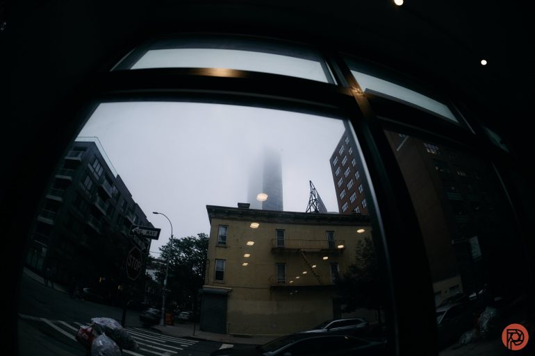 Foggy city scene viewed through a window, with a tall building obscured by mist and streetlights reflected.
