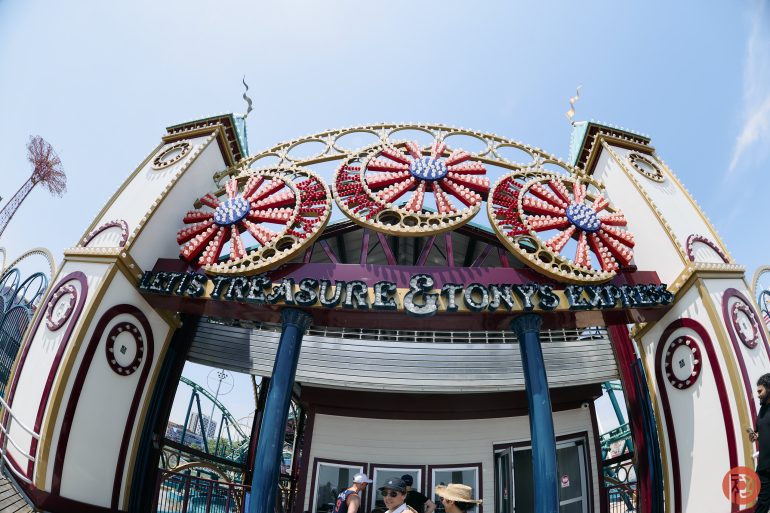 Entrance to a carnival ride called Tonys Express with colorful lights and decorative wheels above.
