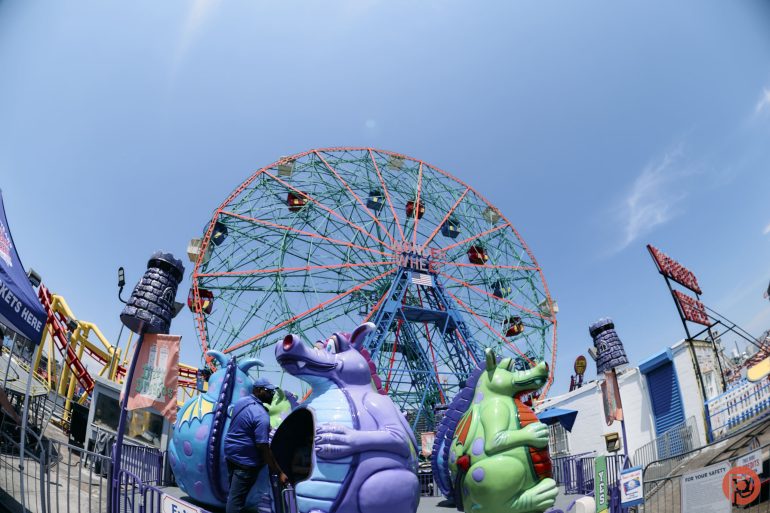 Colorful Ferris wheel and playful dinosaur ride under a bright blue sky at an amusement park.
