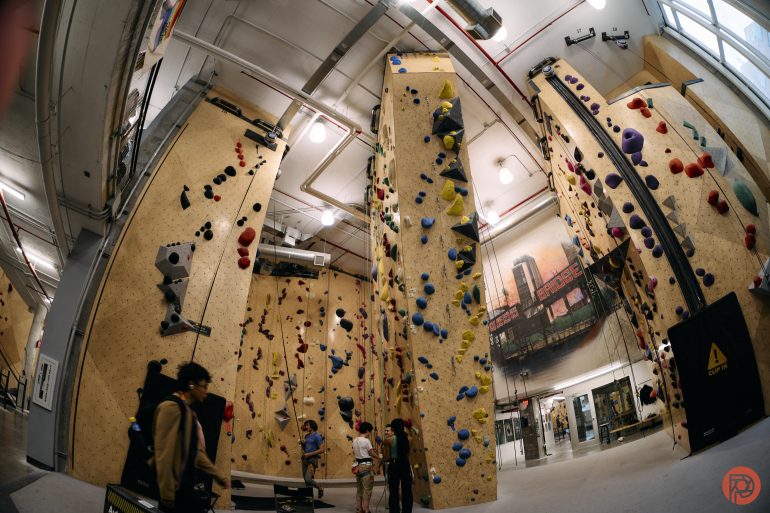 Indoor rock climbing gym with tall climbing walls, colorful holds, and people preparing to climb.