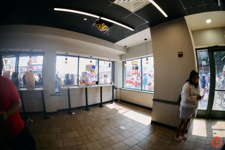 A woman stands near a window in a fast-food restaurant with a busy street scene visible outside.