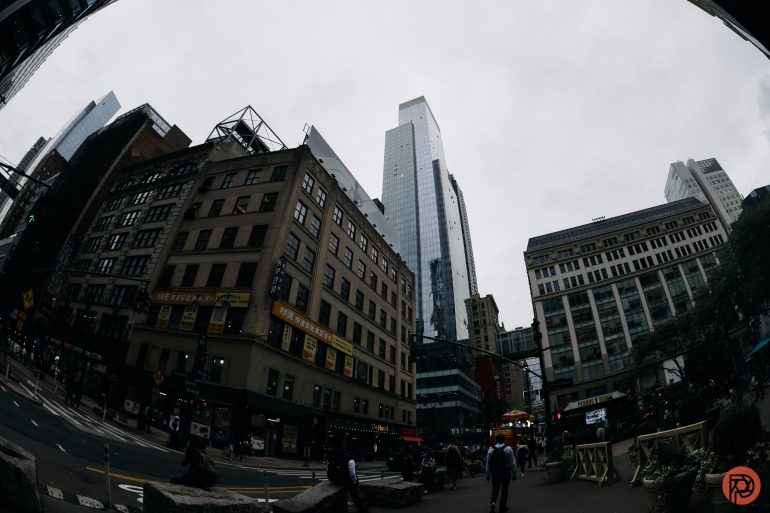 Fisheye view of city buildings and a busy street under a cloudy sky.