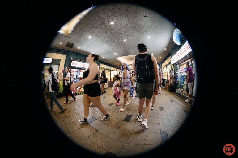 People walk through a busy indoor mall, seen through a circular fisheye lens.