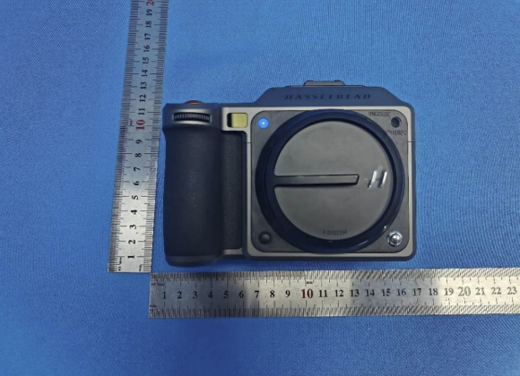 A Hasselblad camera on blue fabric, positioned between two metal rulers showing size in centimeters.