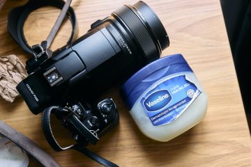 A camera and a jar of Vaseline are placed on a wooden surface in natural light.