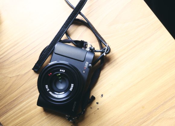 A Sony digital camera with a strap rests on a wooden surface in bright light.