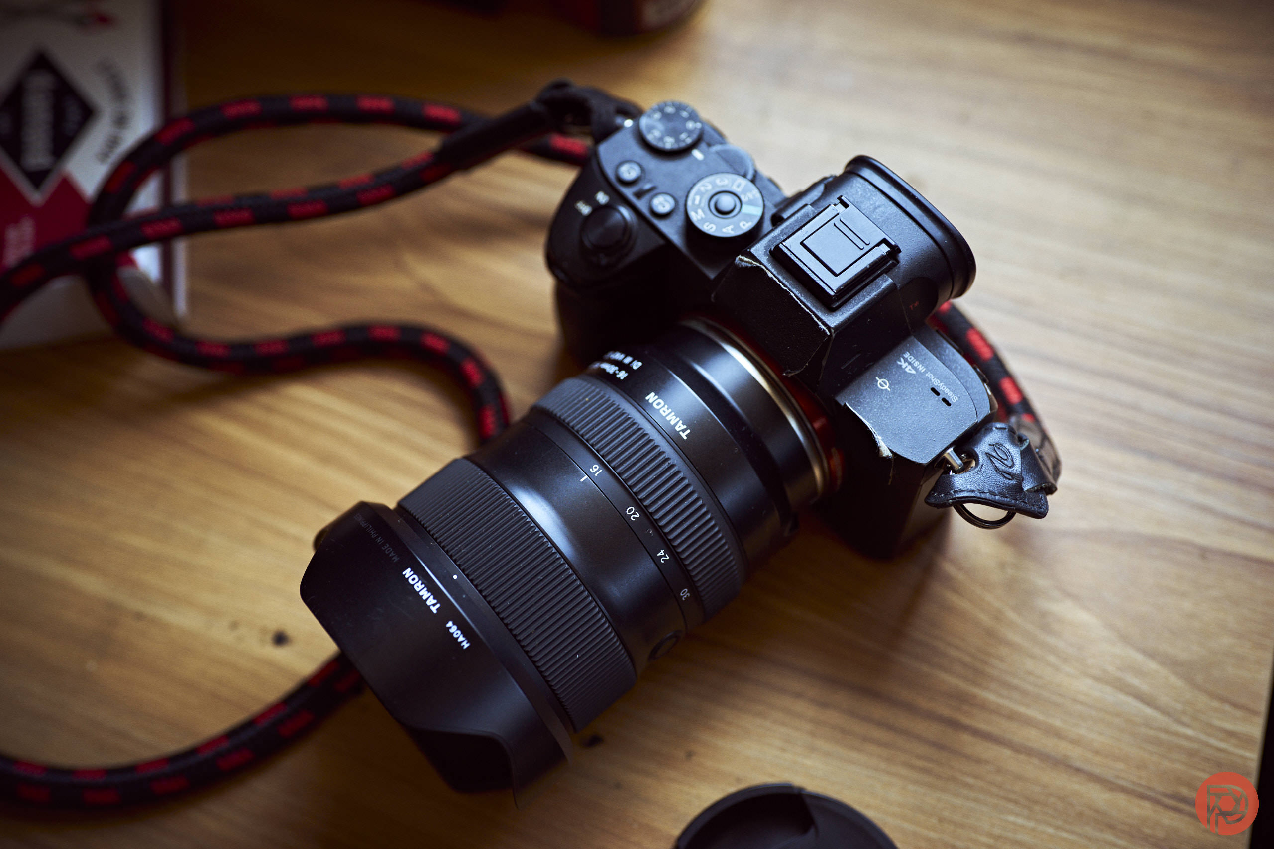 A black digital camera with a large lens rests on a wooden surface with a red and black strap attached.