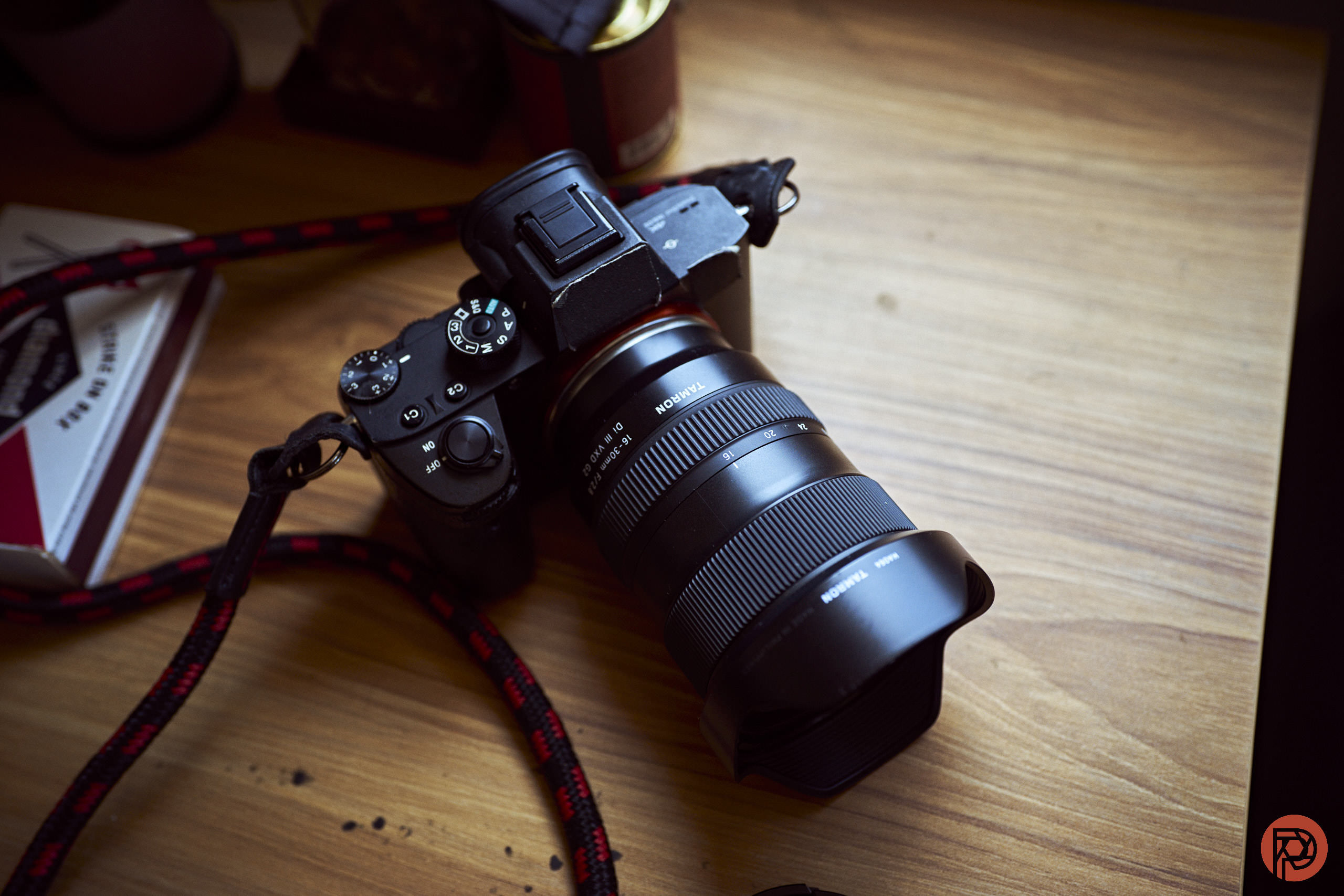A black digital camera with a large lens rests on a wooden desk near books and a cup.