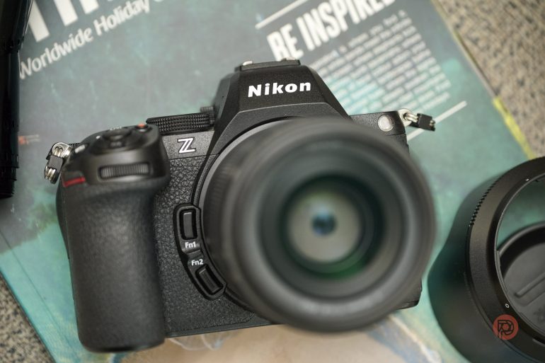 A Nikon Z series camera with a lens attached, placed on a magazine, lens cap nearby.