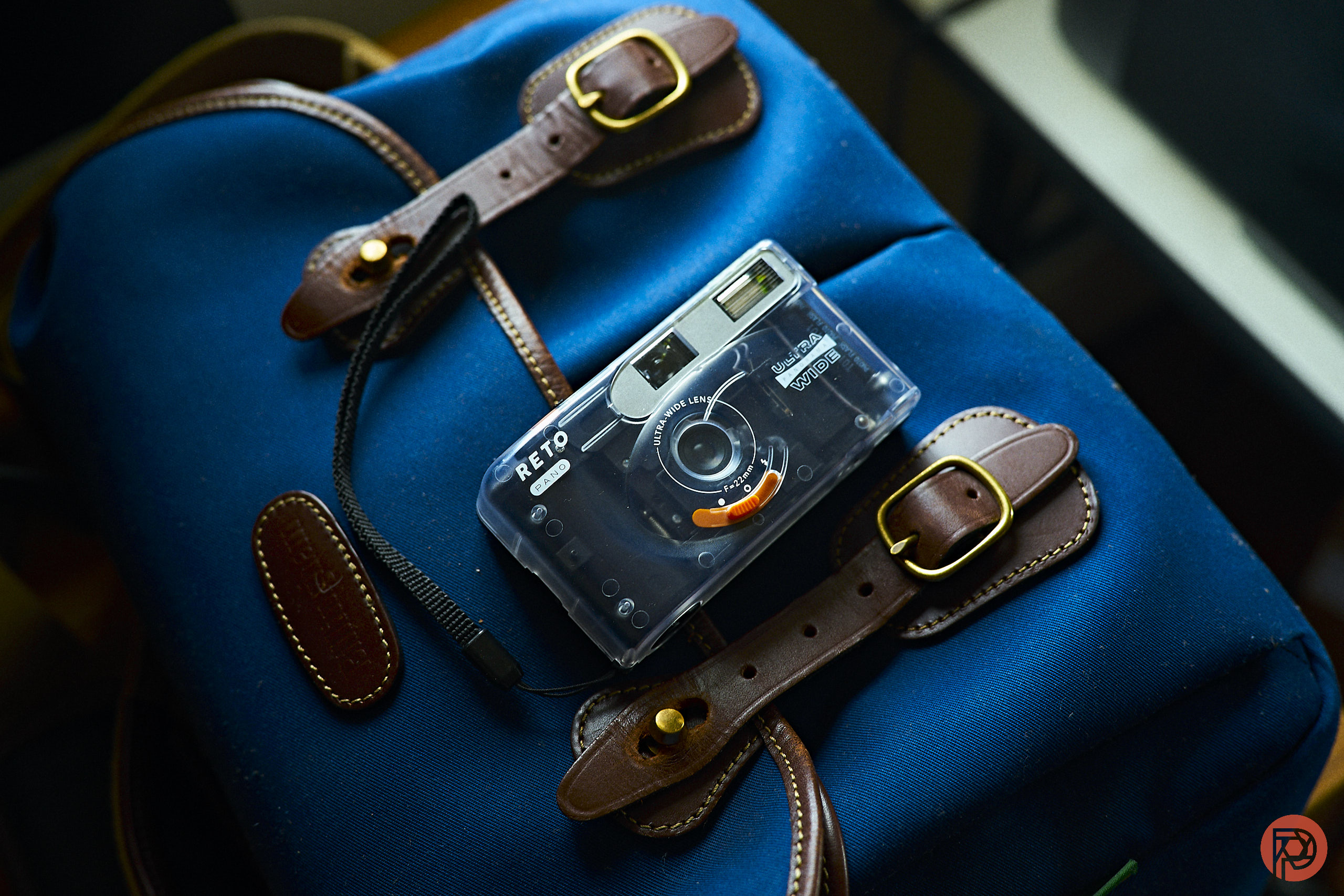 The Best 5 Point-and-Shoot Analog Cameras for Gen Z A retro film camera rests on a blue duffel bag with brown leather straps and brass buckles.