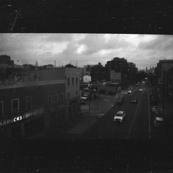 A grainy black-and-white photo of a city street with cars and a Starbucks Coffee on the corner.
