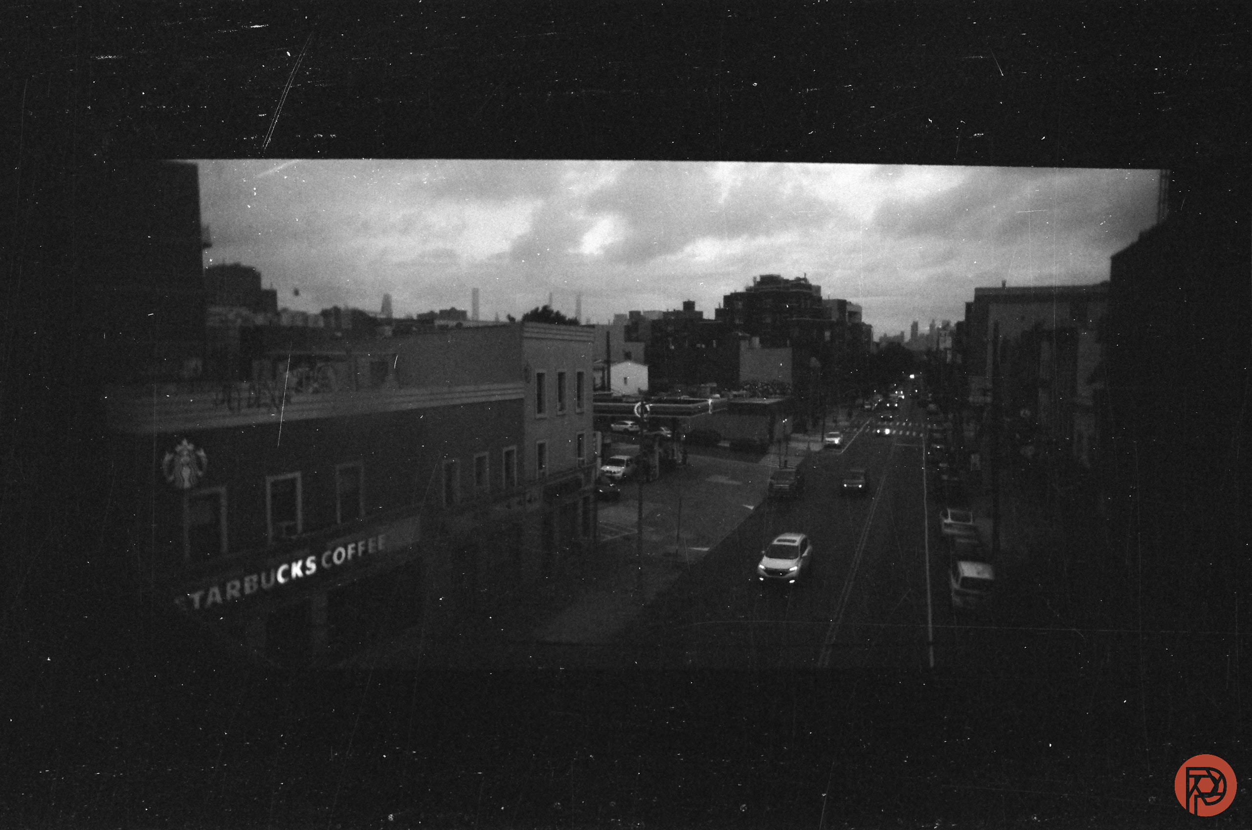 A grainy black-and-white photo of a city street with cars and a Starbucks Coffee on the corner.