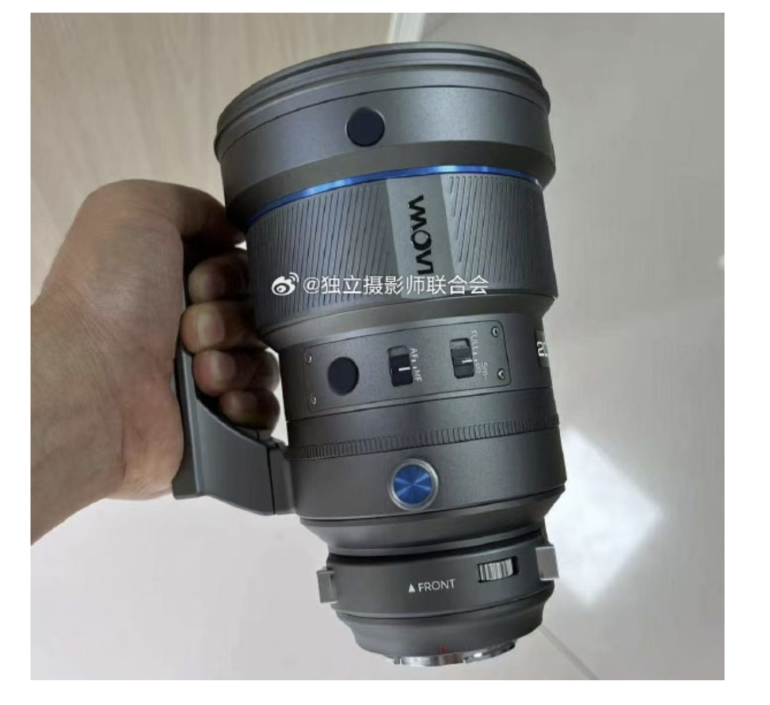 A hand holding a large Laowa camera lens with a handle and multiple adjustment switches.