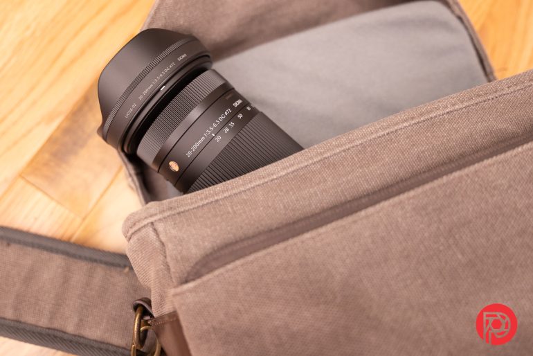 A camera lens partially tucked inside a gray fabric camera bag on a wooden surface.