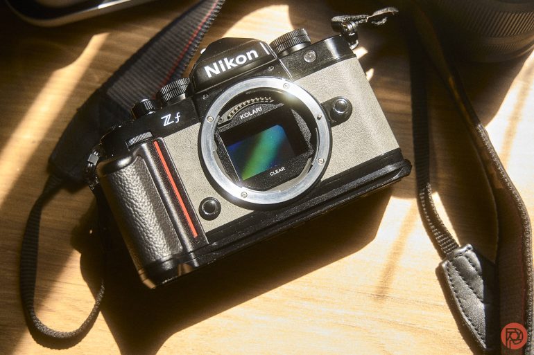 Nikon Zf mirrorless camera without a lens, placed on a wooden surface with sunlight shining on it.